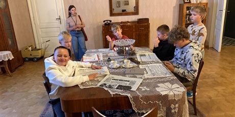 Powiększ grafikę: Grupa dzieci skupiona przy stole wykonuje zadania w jednym z pomieszczeń muzeum.