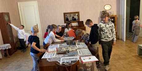 Powiększ grafikę: Grupa dzieci skupiona wokół stołu wykonuje zadanie w jednym z pomieszczeń muzeum. 