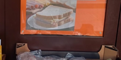 Powiększ grafikę: Pojemnik wypełniony kanapkami. Nad nim znajduje się plakat pokazujący przygotowaną kanapkę.