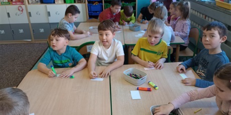 Powiększ grafikę: Dzieci siedzą przy stoliku. Mają przygotowane pisaki i kartki. Dzieci są radosne i chętne do pracy.