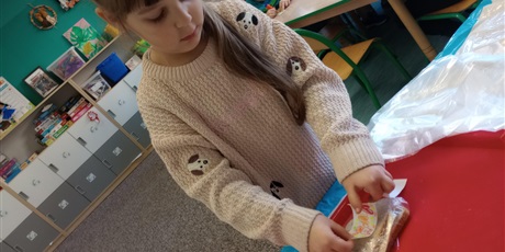 Powiększ grafikę: Dziewczynka nakleja naklejkę z miłym słowem na zapakowaną kanapkę.