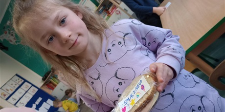 Powiększ grafikę: Dziewczynka prezentuje przygotowaną przez siebie kanapkę wraz z samodzielnie przygotowaną naklejką "Smacznego".