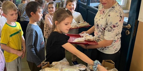 Powiększ grafikę: Grupa dzieci przekłada samodzielnie przygotowane kanapki z tacy do pojemnika. Pojemnik zostanie zawieziony do potrzebujących.