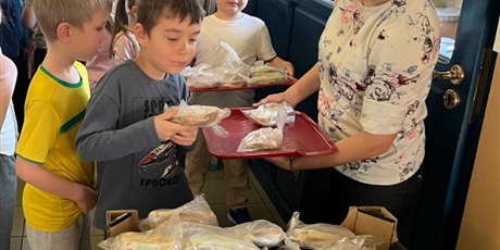 Powiększ grafikę: Grupa dzieci przekłada samodzielnie przygotowane kanapki z tacy do pojemnika. Pojemnik zostanie zawieziony do potrzebujących.