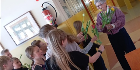 Powiększ grafikę: Grupa uczniów w wieku ok 12 lat wręcza kwiaty nauczycielce. Dzieci są uśmiechnięte a nauczycielka jest wzruszona.