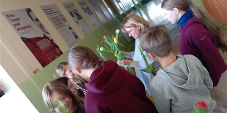 Powiększ grafikę: Grupa uczniów w wieku ok 12 lat wręcza kwiaty nauczycielce. Dzieci są uśmiechnięte a nauczycielka jest wzruszona.