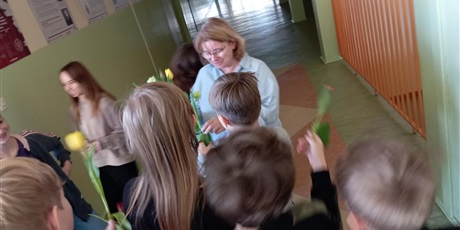 Powiększ grafikę: Grupa uczniów w wieku ok 12 lat wręcza kwiaty nauczycielce. Dzieci są uśmiechnięte a nauczycielka jest wzruszona.