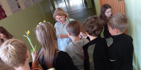 Powiększ grafikę: Grupa uczniów w wieku ok 12 lat wręcza kwiaty nauczycielce. Dzieci są uśmiechnięte a nauczycielka jest wzruszona.