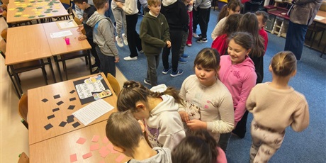 Powiększ grafikę: Dzieci w świetlicy w trakcie zabawy andrzejkowej. Część dzieci chodzi po dywanie lub stoi w kolejce. Część z nich bawi się korzystając z wróżb, które znajdują się na stołach.