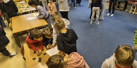 Powiększ grafikę: Dzieci w świetlicy w trakcie zabawy andrzejkowej. Część dzieci chodzi po dywanie lub stoi w kolejce. Część z nich bawi się korzystając z wróżb, które znajdują się na stołach.