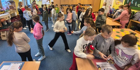 Powiększ grafikę:  Dzieci w świetlicy w trakcie zabawy andrzejkowej. Część dzieci chodzi po dywanie lub stoi w kolejce. Część z nich bawi się korzystając z wróżb, które znajdują się na stołach.