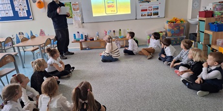 Powiększ grafikę: Dzieci siedzą w kole na dywanie i słuchają prowadzącego.