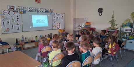 Powiększ grafikę: Grupa dzieci ogląda prezentację na tablicy. Siedzą na krzesełkach i są skupieni.