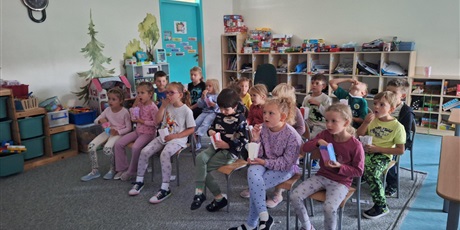 Powiększ grafikę: Grupa dzieci ogląda prezentację na tablicy. Siedzą na krzesełkach, jedzą przekąski.