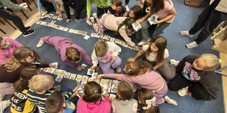 Powiększ grafikę: Duża grupa dzieci układa na dywanie karty przedstawiające różne rodzaje dyni i ich cienie.