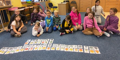 Powiększ grafikę: Grupa dzieci siedząc na dywanie pozuje do zdjęci. Przed nimi leżą karty przedstawiające różne rodzaje dyni i ich cienie.