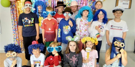Powiększ grafikę: Grupa dzieci z klasy 2A pozuje do zdjęcia. Na głowach mają peruki, kapelusze oraz kolorowe okulary.  Pięcioro dzieci z przodu siedzi na podłodze, pozostali stoją z tyłu.