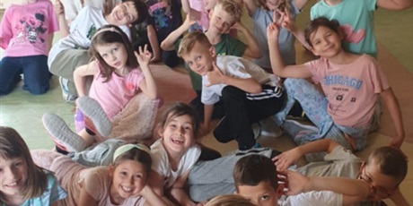 Powiększ grafikę: Grupa dzieci z klasy 1D pozuje do zdjęcia. Część z nich siedzi na podłodze, kilkoro leży. Jedna dziewczynka stoi z tyłu podnosząc ręce do głowy.