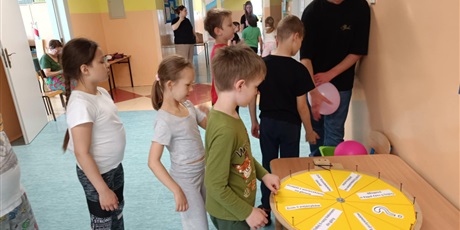 Powiększ grafikę: Kilkoro dzieci stoi w kolejce do koła fortuny, które stoi na stole.