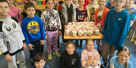 Powiększ grafikę: Grupa dzieci pozuje do zdjęcia. Na środku stoi stół, na którym znajdują się ozdobione "słoiczki mocy" dla mam.