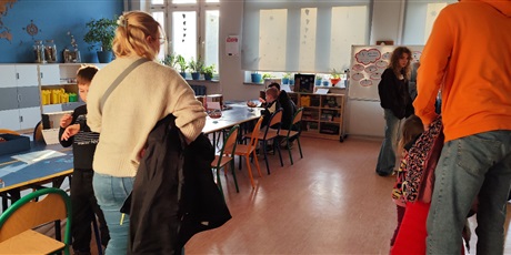 Powiększ grafikę: Na stanowisku Budowanie statku przyszli uczniowie konstruują statki z klocków według instrukcji, rodzice rozmawiają z nauczycielkami.