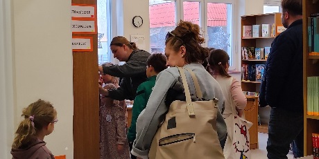 Powiększ grafikę: Przyszli uczniowie wraz z rodzicami odwiedzają bibliotekę szkolną, oglądają księgozbiór, a rodzice rozmawiają z nauczycielami.