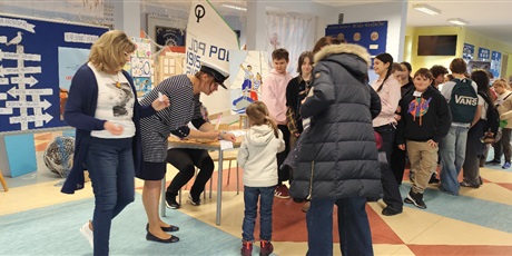 Powiększ grafikę: Przyszli uczniowie szkoły wraz z rodzicami są witani przy wejściu do szkoły. Opiekę nad nimi przejmują szkolni wolontariusze. Gosćie otrzymują mapę podróży i zaczynają zbierać morskie naklejki. 