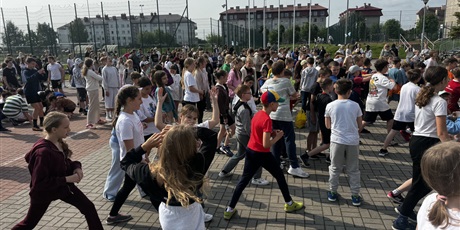 Powiększ grafikę: Duża grupa dzieci w wieku szkolnym wykonuje ćwiczenia na podwórku.