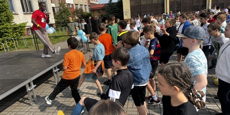 Powiększ grafikę: Dzieci w wieku szkolnym naśladują nauczyciela pokazującego ćwiczenia. Dzieci są ubrane na sportowo. Cieszą się.