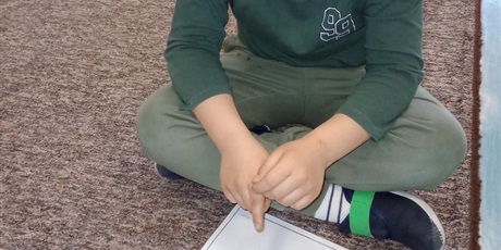 Powiększ grafikę: Chłopiec siedzi na dywanie i prezentuje efekt swojej pracy. W garnuszku są przyklejone monety.