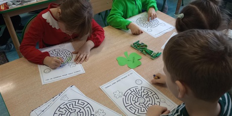 Powiększ grafikę: Dzieci siedzą przy stolikach i pracują w skupieniu. Wyznaczają na kartce drogę w labiryncie.