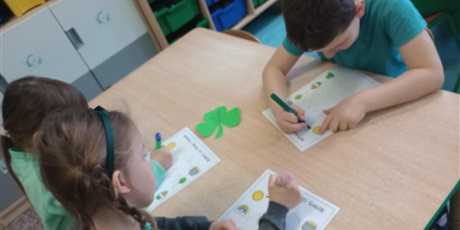 Powiększ grafikę: Dzieci ubrane na zielono rysują pośladzie na kartkach papieru.