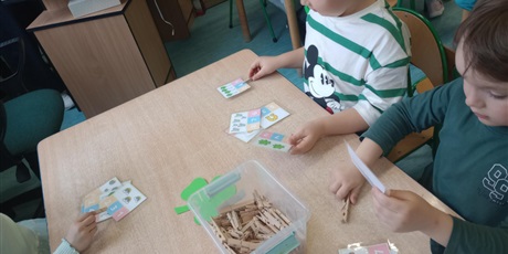 Powiększ grafikę: Dzieci przyczepiają spinacze w miejsce liczby, która mówi ile jest przedmiotów na rysunku.