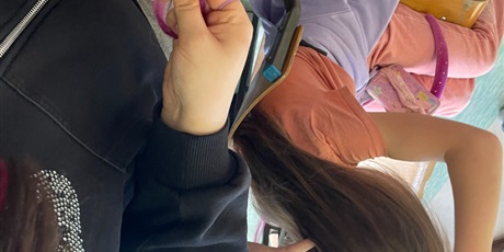 Powiększ grafikę: Wolontariusze zaplatają warkoczyki uczennicom z młodszych klas na korytarzu szkolnym.