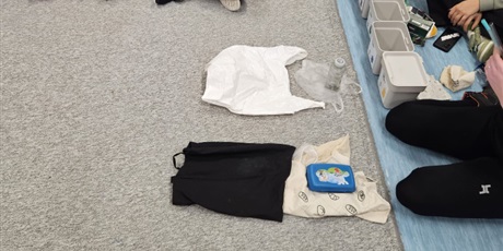 Powiększ grafikę: Przed osobą prowadzącą leżą różne materiały: torba plastikowa, torba materiałowa, pudełko.