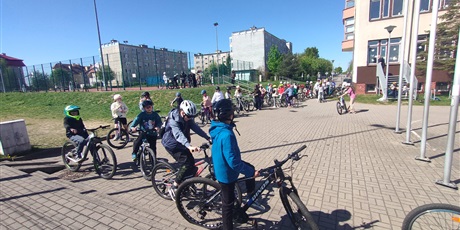 Powiększ grafikę: Grupa dzieci w kaskach stoi z rowerami przed szkołą i przygotowuje się do egzaminu na kartę rowerową.