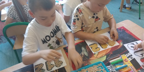 Powiększ grafikę: Dwóch chłopców siedzi przy stoliku, przy użyciu plasteliny i kulek grochu ozdabiają nr alarmowy 112.