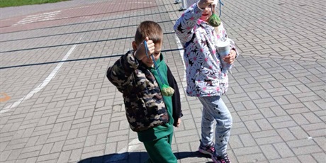 Powiększ grafikę: Na zdjęciu jest dwoje dzieci w wieku 6 lat. Trzymają w rękach zielone siatki z pokarmem dla zwierząt.