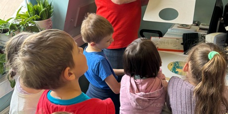 Powiększ grafikę: Dzieci w wieku 7 lat słuchają pracownika Radia Gdańsk, który opowiada o swojej pracy. Pracownik ma na sobie czerwoną koszulkę z krótkim rękawem. W ręce trzyma sprzęt do miksowania płyt.