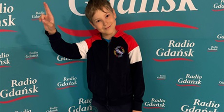 Powiększ grafikę: Siedmioletni chłopiec pozuje na tle turkusowej ścianki z napisem Radio Gdańsk. Chłopiec ma na sobie czarny dres,  z kolorowymi czerwono-białymi pasami.  Na spodniach ma kolorowe litery.
