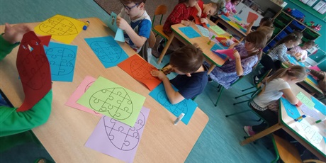 Powiększ grafikę: Dzieci w wieku lat 7 pracują przy stolikach. Na pierwszym planie widać chłopców, którzy wycinają nożyczkami.