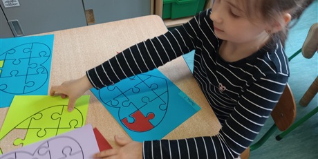 Powiększ grafikę: Dziewczynka, lat 7, w czarnej w białe paski koszulce, z długim rękawem dotyka kolorowych kartek. Prawą dłonią dziewczynka chwyta zieloną kartkę. Lewa dłoń dziewczynki łapie kartkę fioletową.