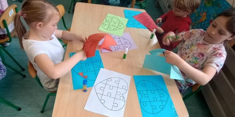 Powiększ grafikę: Dzieci w wieku lat 7 wycinają kolorowe kartki. Grupa pracuje w skupieniu przy stolikach.