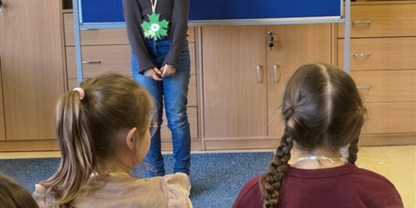 Powiększ grafikę: Dziewczynka w ciemnej bluzce stoi zwrócona przodem do publiczności.  Za nią stoi granatowa tablica z kolorową dekoracją i napisem I Edycja Konkursu Recytatorskiego „W kręgu poezji Ludwika Jerzego Kern