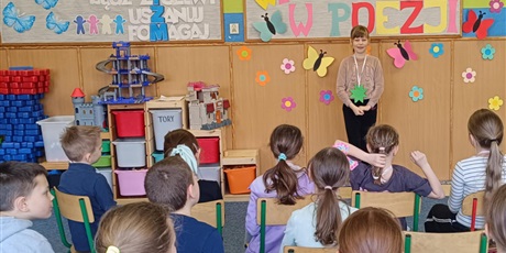 Powiększ grafikę: Grupa dzieci siedzi tyłem.  Dziewczynka stoi przodem i recytuje wiersz.