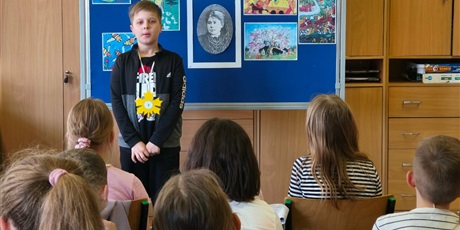 Powiększ grafikę: Chłopiec w ciemnej bluzie stoi zwrócony przodem do publiczności.  Za nim stoi granatowa tablica z kolorową dekoracją i napisem II Edycja Konkursu Recytatorskiego „W świecie Marii Konopnickiej”.