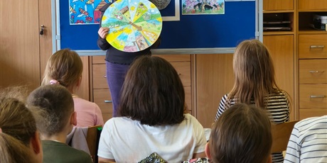 Powiększ grafikę: Dziewczynka stoi zwrócona przodem do publiczności.  W rękach trzyma kolorowe koło. Za nią stoi granatowa tablica z kolorową dekoracją i napisem II Edycja Konkursu Recytatorskiego „W świecie Marii Kono