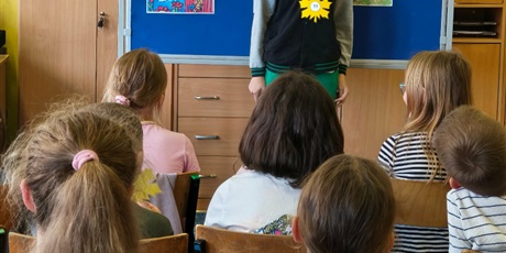 Powiększ grafikę: Chłopiec w ciemnej bluzie stoi zwrócony przodem do publiczności.  Za nim stoi granatowa tablica z kolorową dekoracją i napisem II Edycja Konkursu Recytatorskiego „W świecie Marii Konopnickiej”.