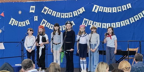 Powiększ grafikę: Siedem osób stoi na scenie. Są to dzieci w wieku 10-12 lat. Są przebrani za piratów. Stoją przed mikrofonami.