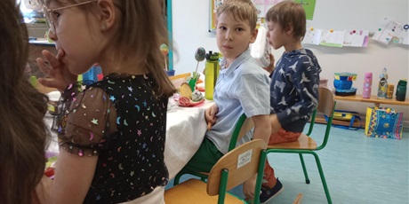 Powiększ grafikę: Dzieci siedzą przy stole. Jeden chłopiec odwrócony jest od stołu i patrzy w obiektyw.